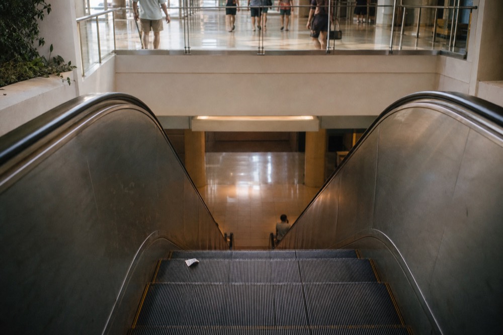Escalator descending toward a shopping mall basement aquarium entrance, no text, no logos, no people.