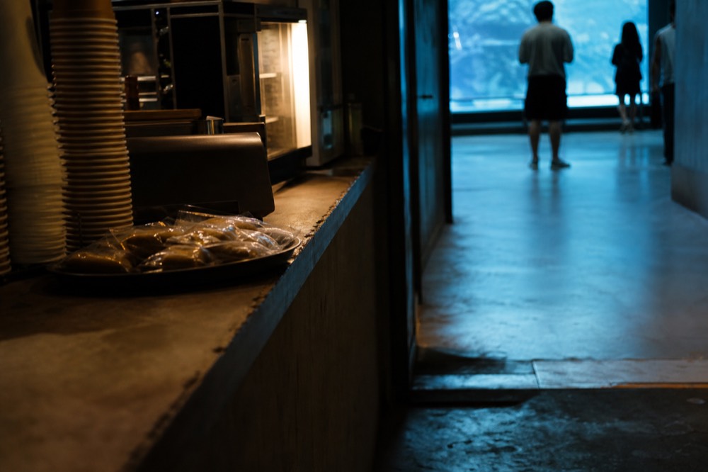 A small cafe counter with drinks and snacks displayed beside a dimly lit aquarium corridor, no text, no logos, no people.