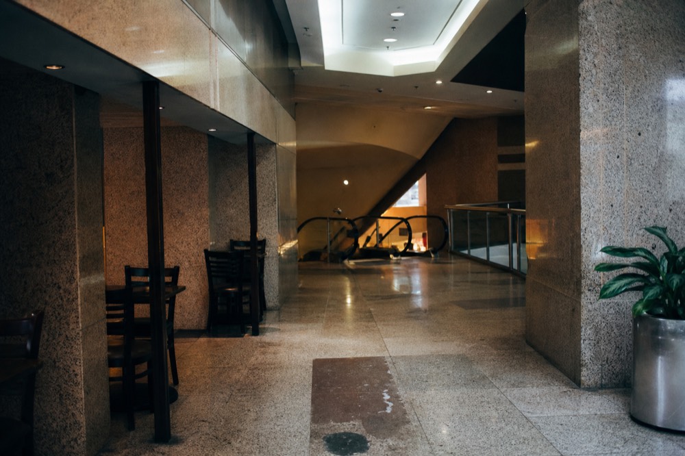 A bright mall corridor with seating areas and escalators leading down to a basement food level, no text, no logos, no people.