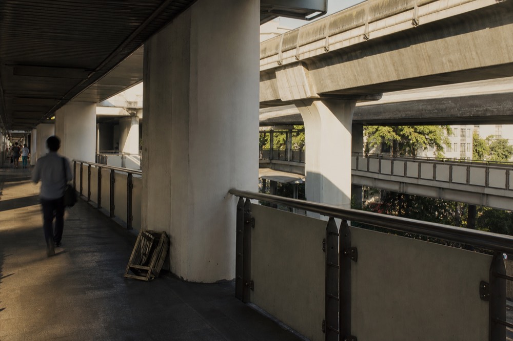 A covered Bangkok walkway with Skytrain tracks overhead, no text, no logos, no people.