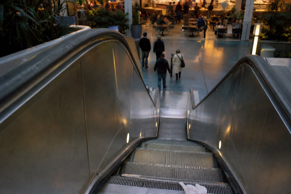 Escalator descending into a shopping mall basement near a food court, no text, no logos, no people