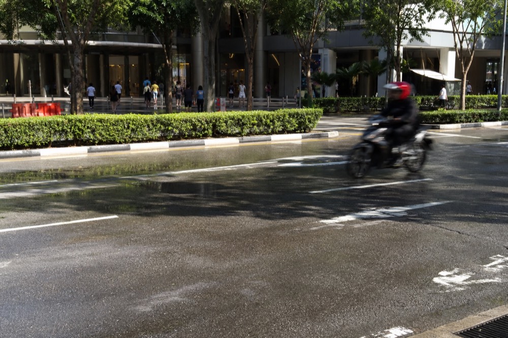 City road with a shopping mall entrance and a turning lane, no text, no logos, no people.