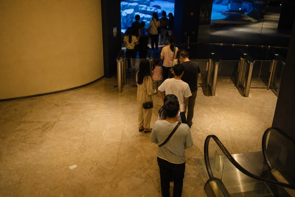 A ticket counter queue in a shopping mall basement with an aquarium entrance behind it, no text, no logos, no people